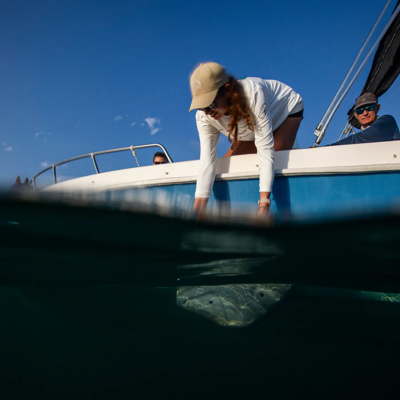 Marine Lab team member reaching from a boat over a split above/below water view